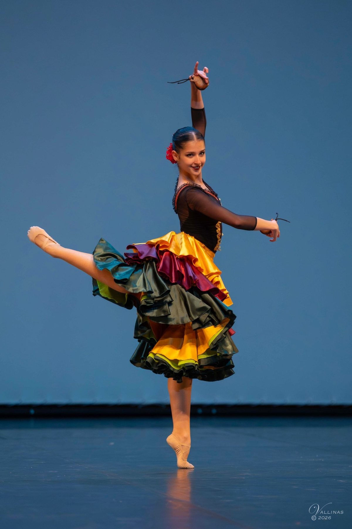 Bailarina de bolera con falda de volantes de colores y castañuelas en arabesque
