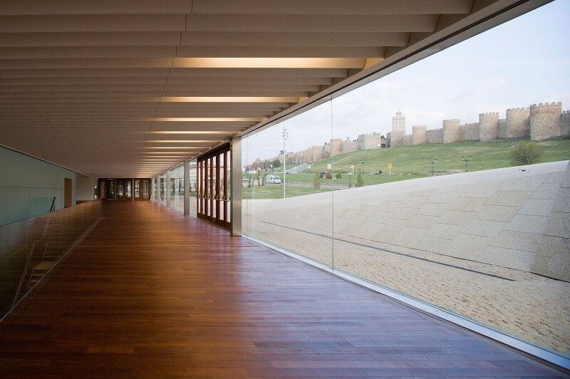 Galería interior de Lienzo Norte con suelo de madera y una gran cristalera con vistas a la muralla de Ávila