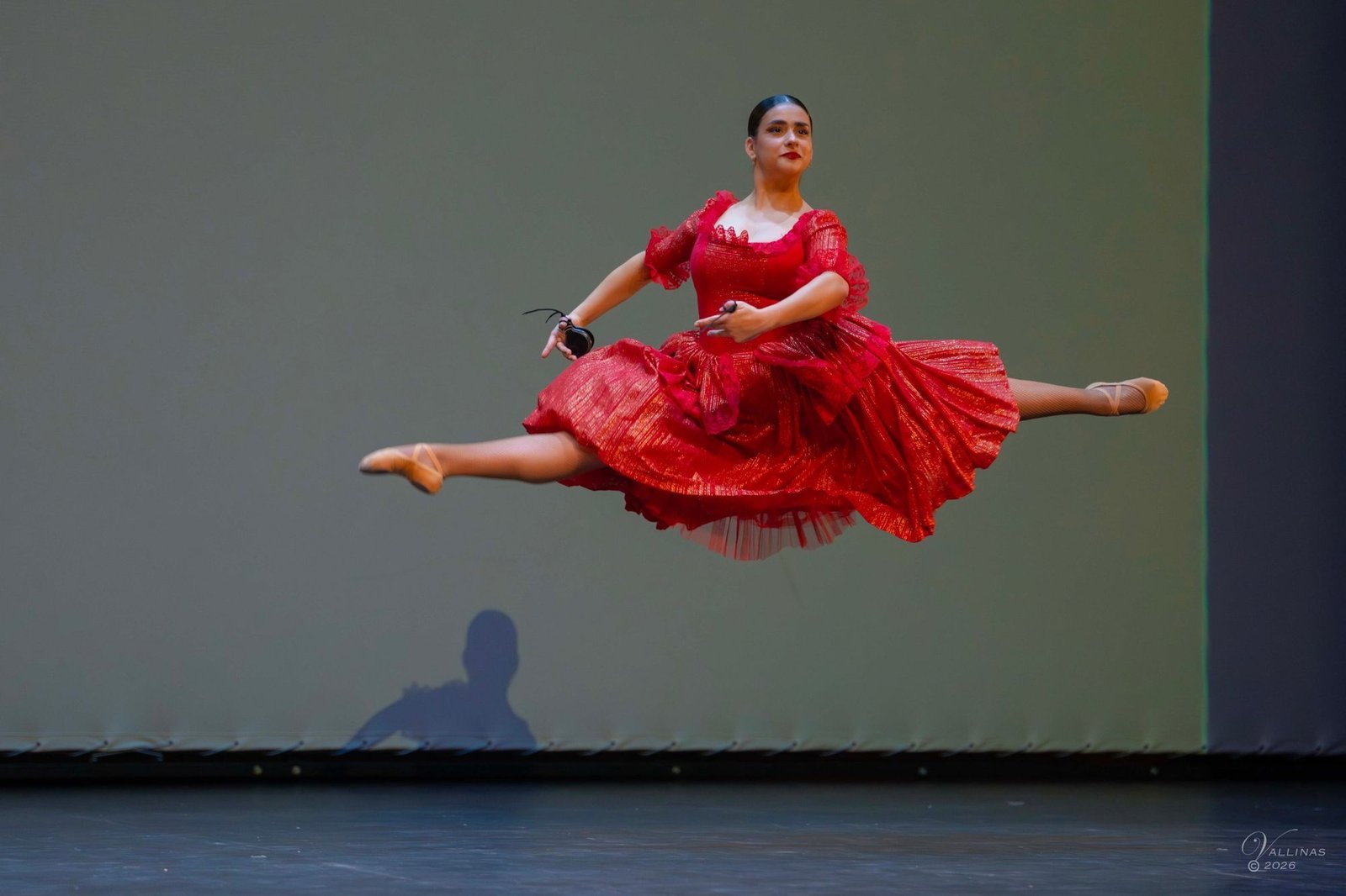 Bailarina de escuela bolera con vestido rojo suspendida en el aire en un gran salto con castañuelas